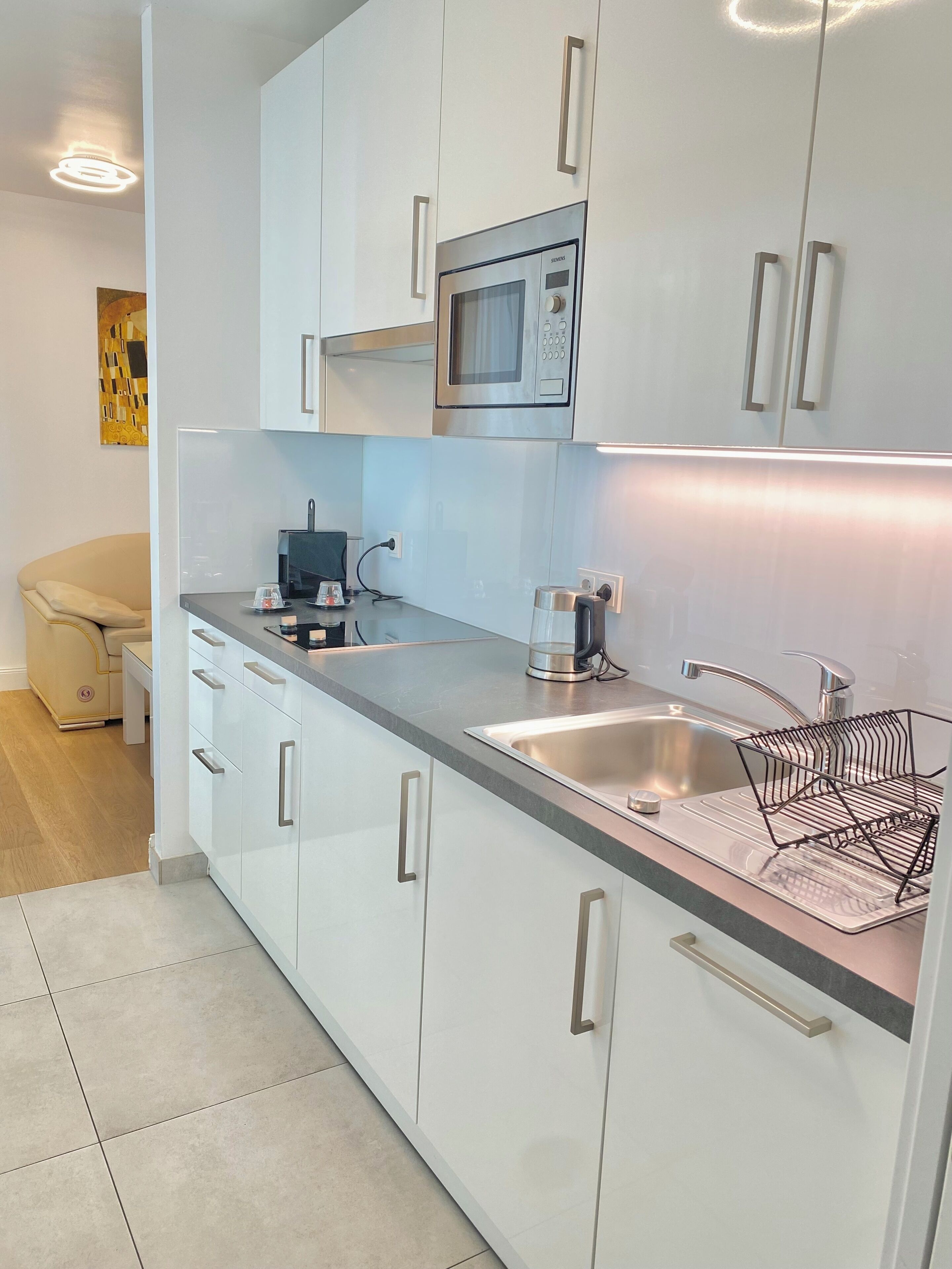 A modern kitchen with white cabinets, a stainless steel sink, a microwave, and a coffee maker.