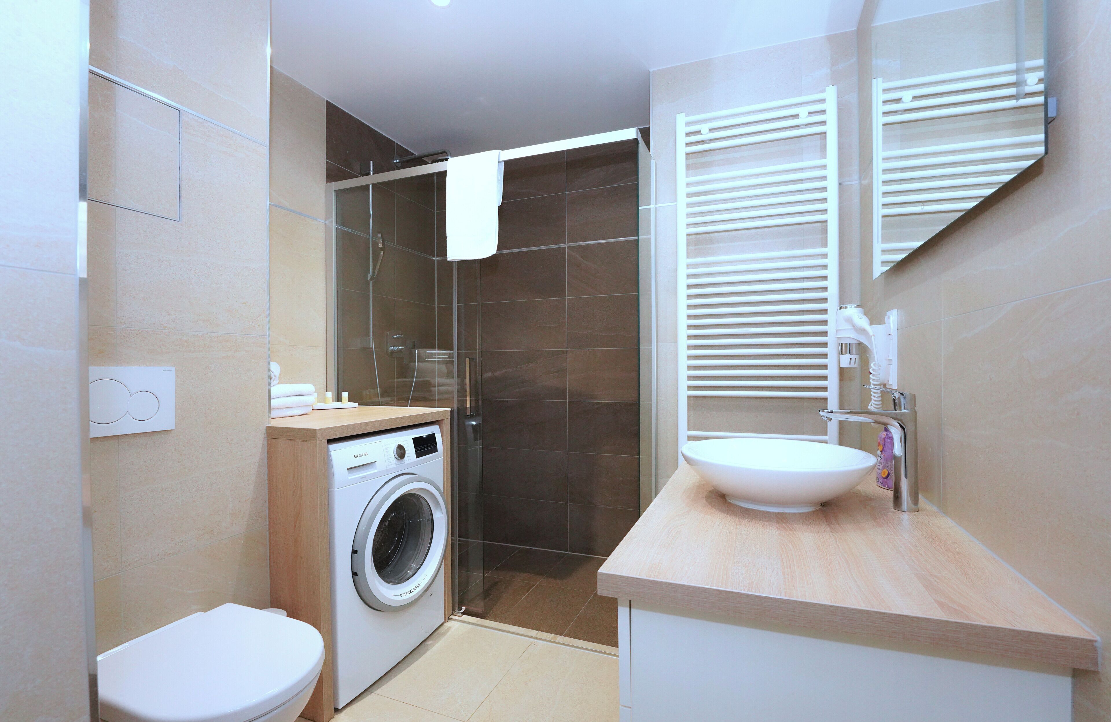A modern bathroom with a washing machine, toilet, and sink.
