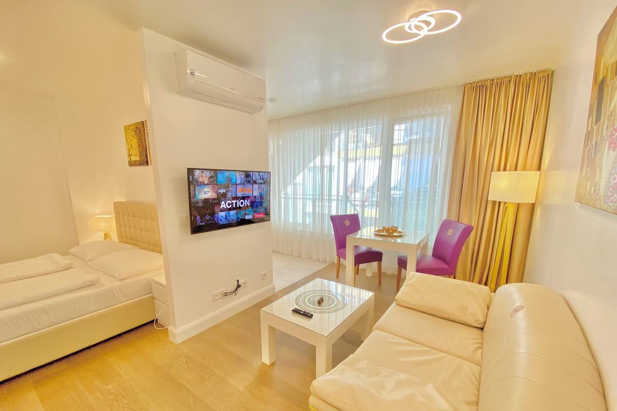 A modern hotel room with a flat-screen TV mounted on the wall, a sofa, a small table, and a chair.