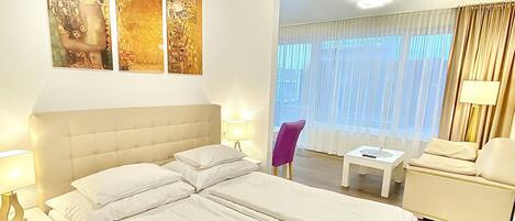 A modern hotel room with a large bed, bedside tables, a chair, and artwork on the wall.