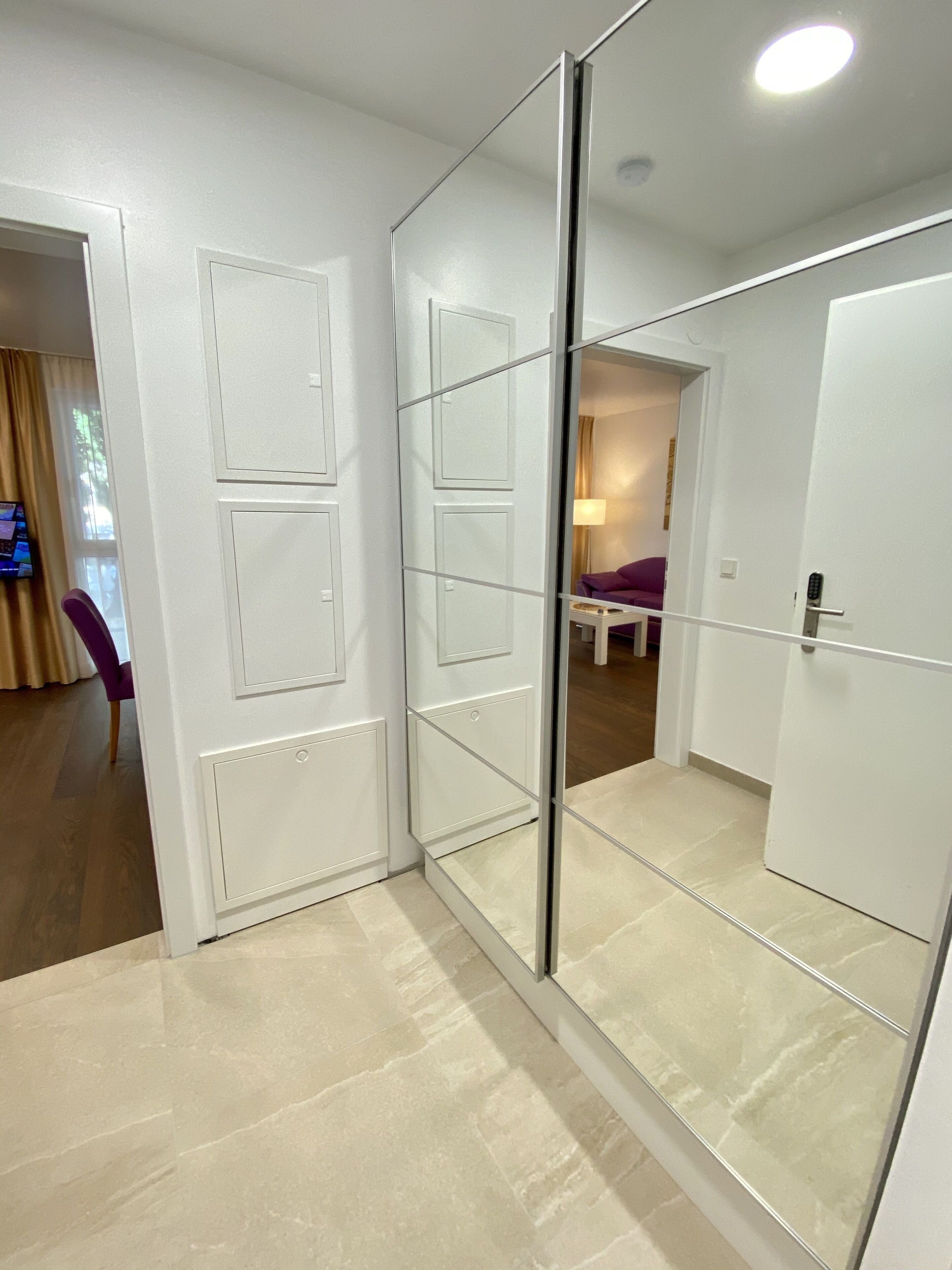 Una camera d'albergo moderna con una porta scorrevole in vetro che dà su un soggiorno, una televisione a schermo piatto e una poltrona viola.