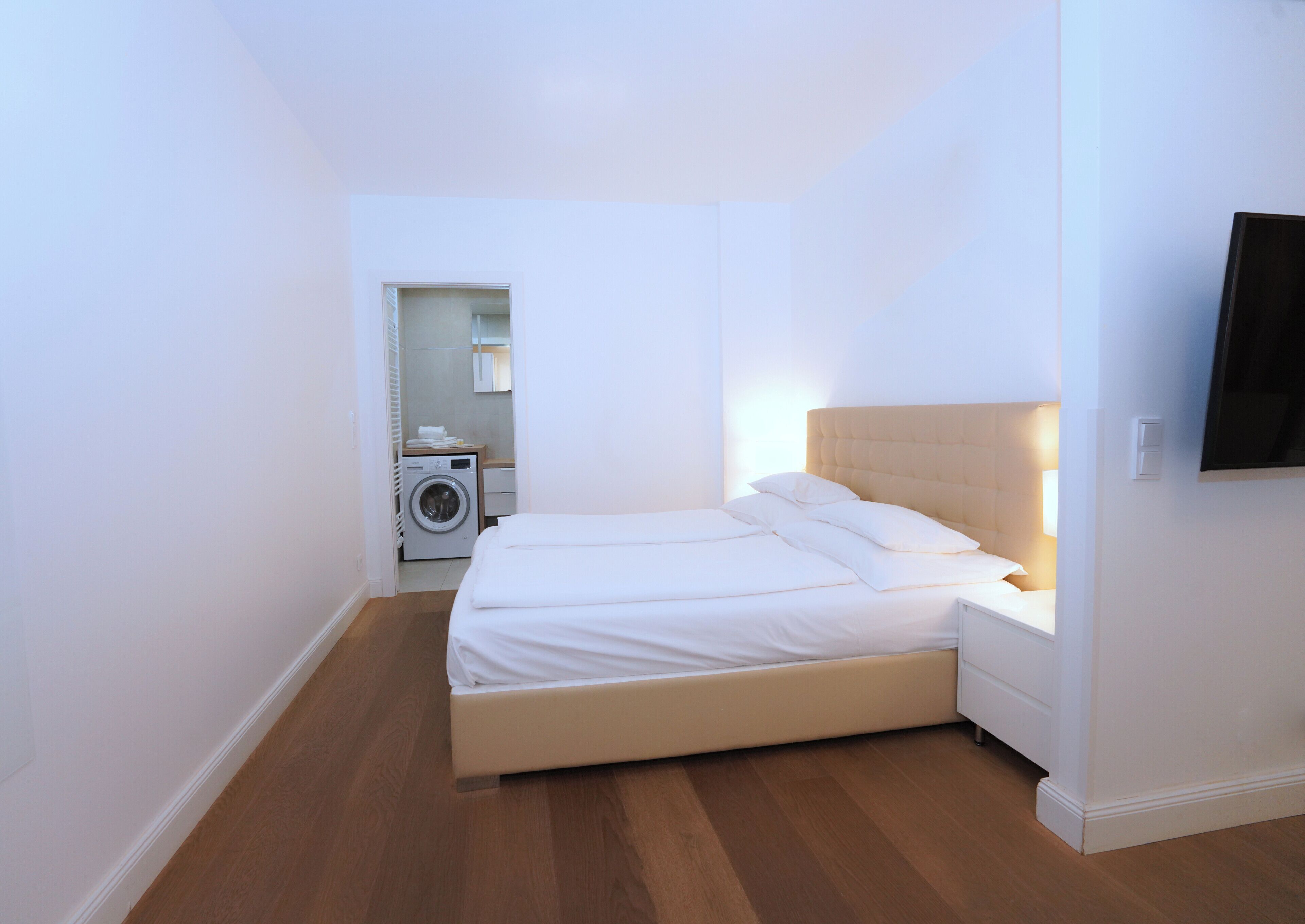Une chambre avec un lit, un lave-linge et un téléviseur fixé au mur.