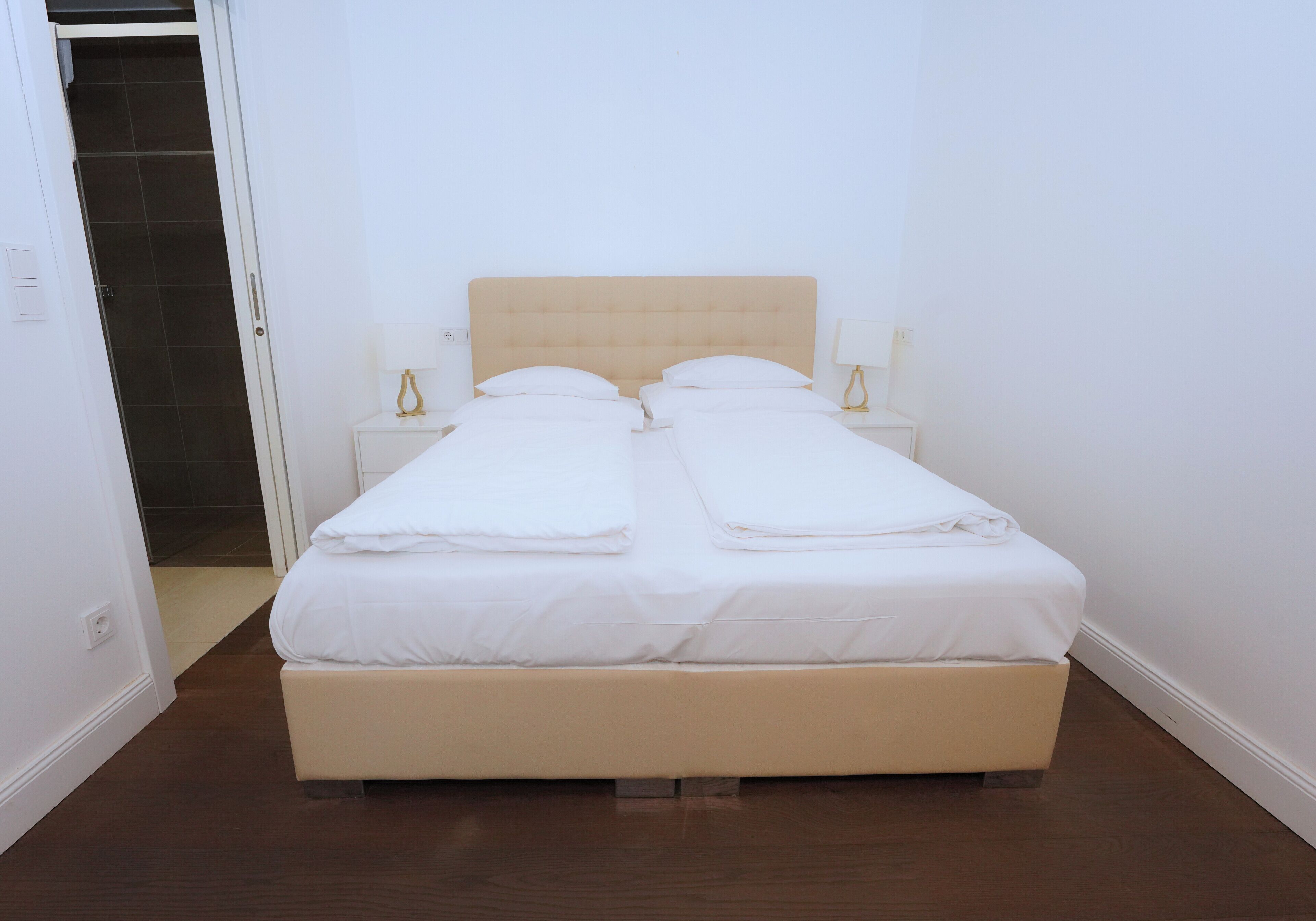 A double bed with a wooden headboard, two bedside tables with lamps, and a door leading to a tiled area.