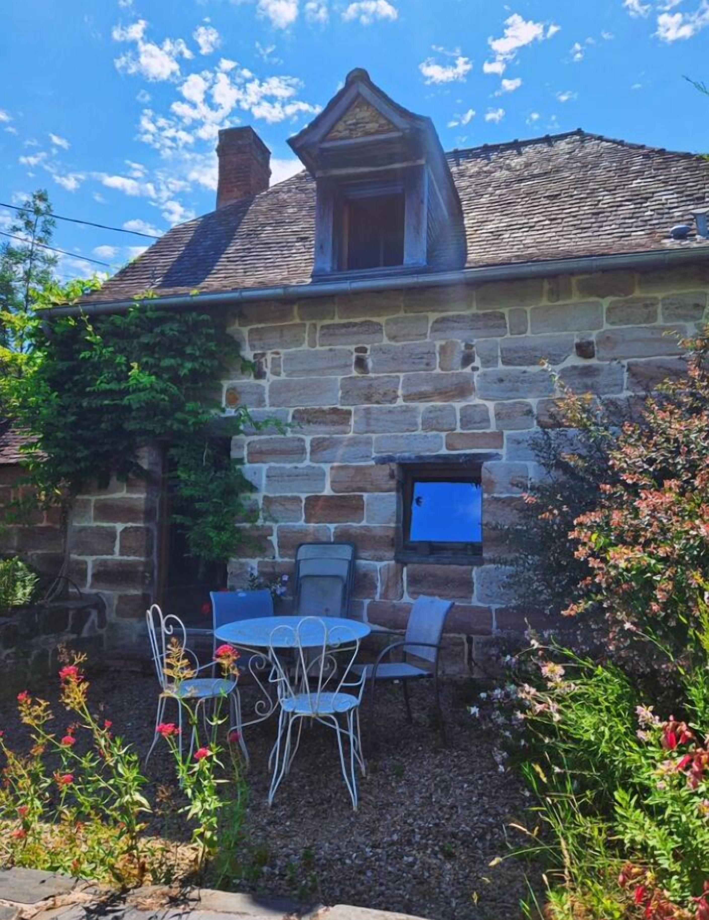 Una casa de piedra con un pequeño balcón, una ventana y una mesa con sillas afuera.