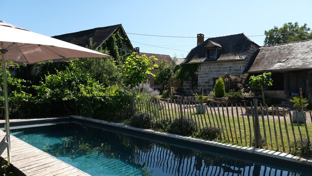 Una piscina rectangular con cubierta de madera, rodeada por una valla de madera y abundante follaje.