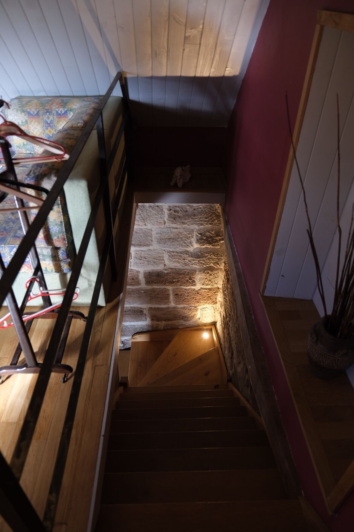 Eine Holztreppe mit einer Steinwand oben, die zu einem Raum mit roter Wand und Holzboden führt.