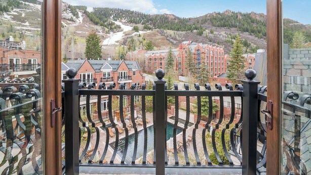 A view from a balcony with a metal railing, overlooking a town with buildings, a river, and a mountain in the background.