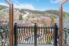 Blick vom Balkon mit Metallgeländer auf eine Stadt mit Gebäuden, einem Fluss und einem Berg im Hintergrund.
