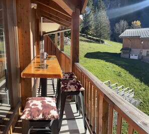 A wooden deck with a table and chairs, overlooking a grassy area and a building in the background. - 50m from ski slopes, 4th floor, swimming pool, sauna, hammam, balcony, parking, tv, ski locker, 32m² (Pralognan-la-Vanoise)