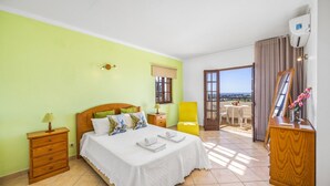 Une chambre à coucher comprenant un lit, une table de chevet, une commode, une fenêtre et un balcon avec vue.