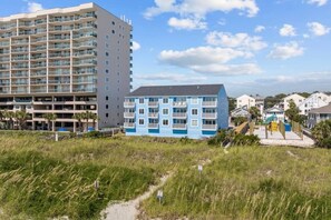 A coastal building with multiple floors, a flat roof, and a pathway leading to a playground. - 6 Beds, Pool, Corner View- 3 Bdrm Duneside Dream (North Myrtle Beach)