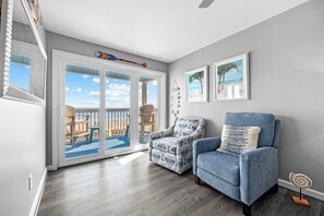 A room with a view through a sliding glass door, a blue armchair, a patterned armchair, and two framed pictures on the wall. - 6 Beds, Pool, Corner View- 3 Bdrm Duneside Dream (North Myrtle Beach)