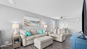 Ein modernes Wohnzimmer mit grauem Sofagarnitur, einem Couchtisch, einer TV-Konsole und einem Deckenventilator.