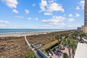 A coastal view with a beach, a boardwalk, and a building with balconies overlooking the ocean. - 6 Beds, Pool, Corner View- 3 Bdrm Duneside Dream (North Myrtle Beach)