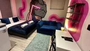 A modern bedroom with a bed, two sofas, a desk, and a wall-mounted shelf.