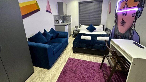 A compact hotel room with a bed, a sofa, a desk, and a kitchenette.