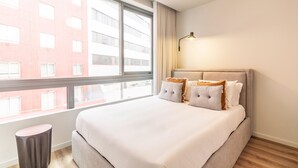 A hotel room with a large bed, a bedside lamp, and a view of a red building through the window. - RUAH Q - Quiet Flat by LovelyStay (Vila Nova de Gaia)