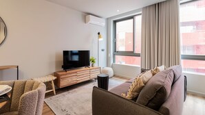 A modern living room with a flat-screen TV, wooden furniture, a round ottoman, and a large window with curtains. - RUAH Q - Quiet Flat by LovelyStay (Vila Nova de Gaia)
