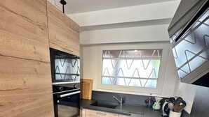 Una cocina moderna con armarios de madera, encimera negra, horno empotrado y ventana con vidrio esmerilado.