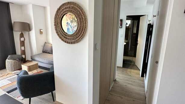 Una sala de estar moderna con un sofá, una mesa de centro y una lámpara. Se ve un pasillo que conduce a otra habitación.