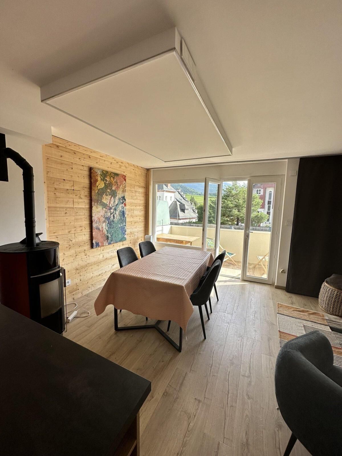 Ein modernes Zimmer mit einer Holzwand, einem großen Fenster, einem Tisch mit Stühlen und einem schwarzen Heizkörper.