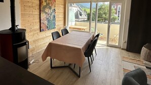 Una habitación moderna con una pared de madera, un ventanal grande, una mesa con sillas y un calefactor negro.