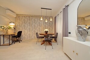 A dining area with a round table, four chairs, a vase of flowers, pendant lights, a white cabinet, and a large mirror. - 4BNB - Ponte Milvio Apartment (Rome)