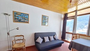 A room with a dark blue sofa, a wooden chair, a table, and two framed pictures on the wall. - 200 meters from the ski slopes, 3rd floor, balcony, TV, ski locker, 50 m², Pra Loup (Uvernet-Fours)