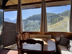 Ein gemütliches Blockhaus-Interieur mit einem Holztisch und -stühlen, einer Couch und einem großen Fenster mit Blick auf eine bewaldete Berglandschaft.