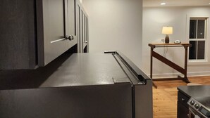 A modern kitchen with dark cabinetry, a stainless steel refrigerator, and a wooden table with a lamp. - *Downtown Middlebury Waterfall Studio Apartment* (Middlebury)