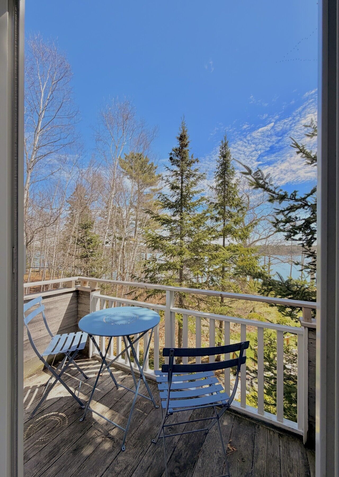 A wooden deck with a table and chairs, overlooking a forest and a body of water.
