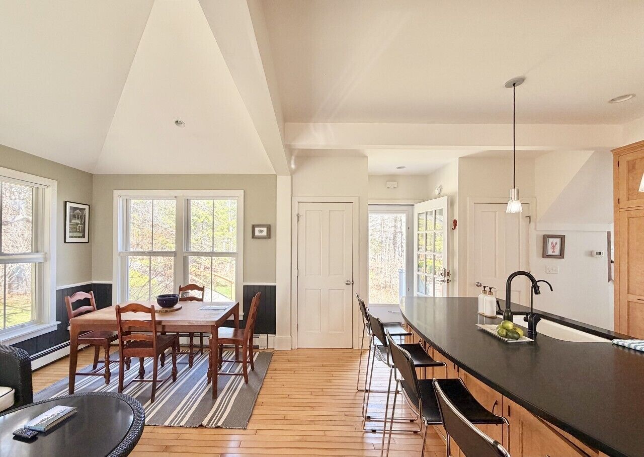 A spacious kitchen with a long island, wooden flooring, and large windows.