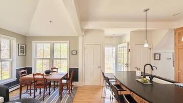 A spacious kitchen with a long island, wooden flooring, and large windows.