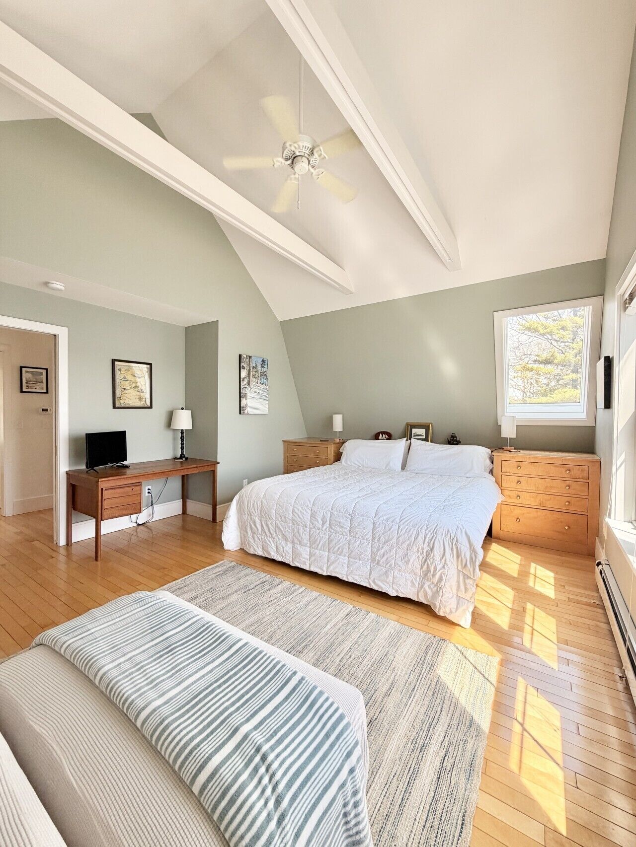 A bedroom with a bed, bedside tables, a desk, a chair, a ceiling fan, and a window.