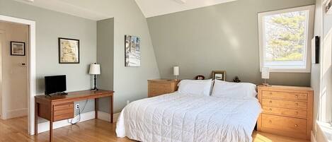 A bedroom with a bed, bedside tables, a desk, a chair, a ceiling fan, and a window.