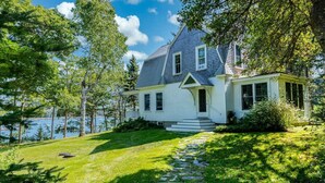 A house with a stone pathway leading to the front door, surrounded by lush greenery and a lake view. - Mere Point Sunrise Views at Eastern Shore! (Brunswick)