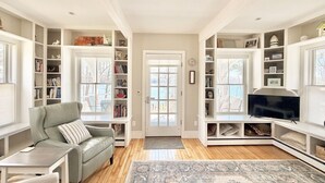 A living room with a sofa, a coffee table, a television, and built-in shelving with books and decorative items. - Mere Point Sunrise Views at Eastern Shore! (Brunswick)