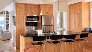 A modern kitchen with wooden cabinets, stainless steel appliances, and a central island with bar stools. - Mere Point Sunrise Views at Eastern Shore! (Brunswick)