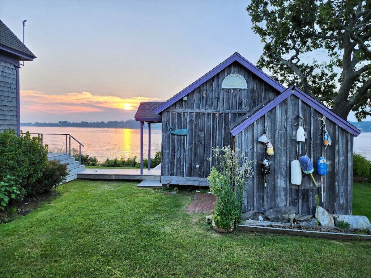 Eine Holzhütte mit Veranda, einer kleinen Terrasse und Bojen an der Seite.