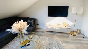 Ein modernes Wohnzimmer mit einem dunkelgrauen Sofa, einem Glastisch, einem flachbildfernseher an der Wand und einer Stehlampe.