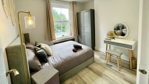 Ein modernes Schlafzimmer mit Bett, Nachttisch, Spiegel und einem Fenster mit Vorhängen.