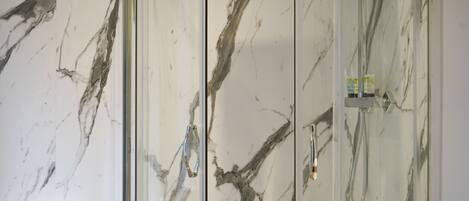 A bathroom with a marble wall, a toilet, and a shower with a glass door.