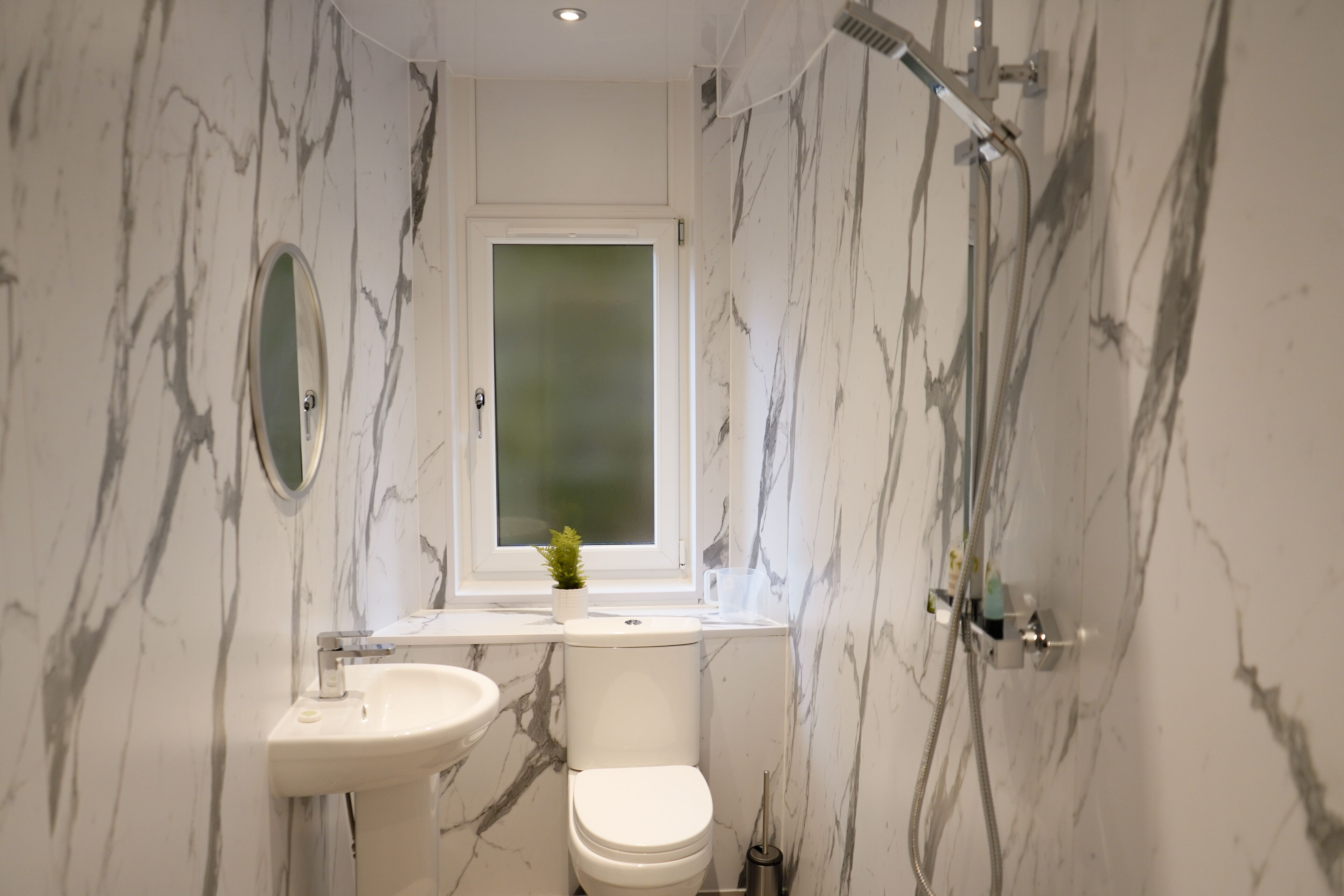 A bathroom with a marble wall, a toilet, a sink, and a window.