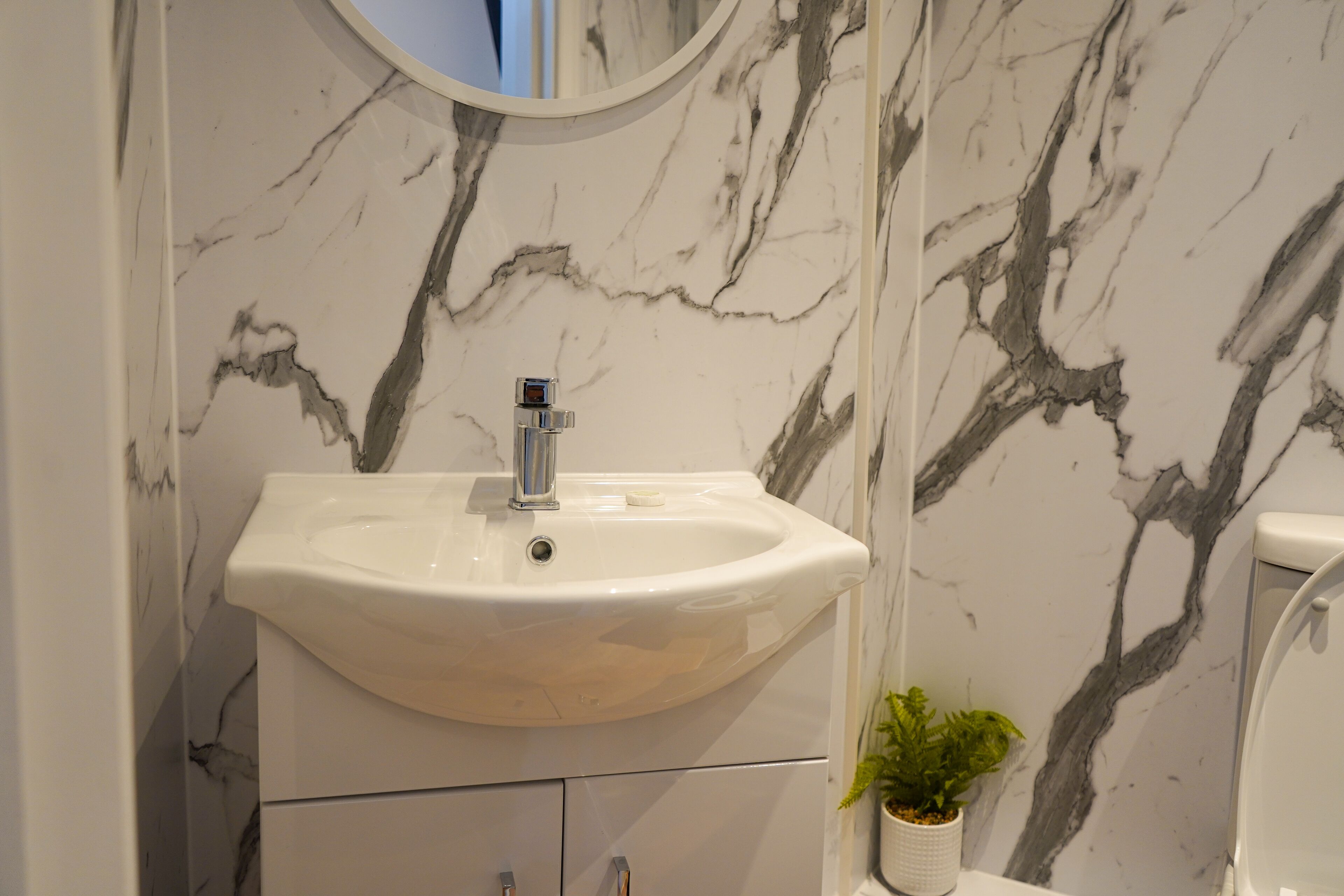 A bathroom with a white marble sink, a mirror above it, and a potted plant beside the toilet.