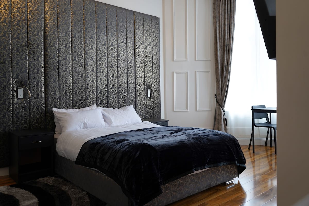 Un dormitorio moderno con una cama grande, suelo de madera oscura y un panel de pared texturizado.