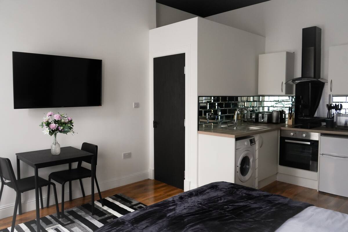 Una cocina moderna con lavadora, horno y zona de comedor con una mesa y sillas negras.