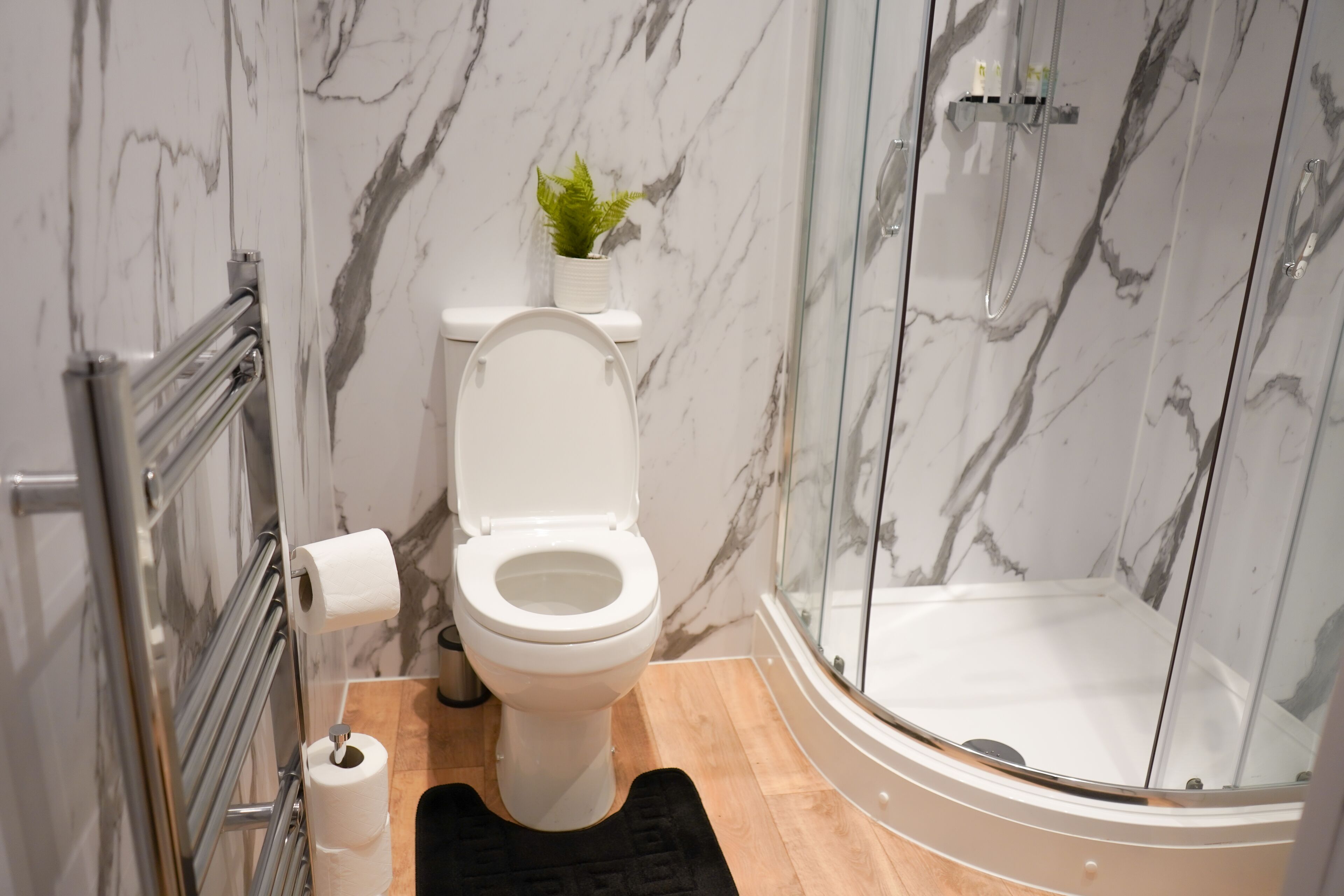 Un baño con inodoro, ducha y pared de mármol.