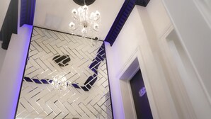 Un interior moderno con una pared de diseño geométrico, una araña y una escalera con detalles azules.