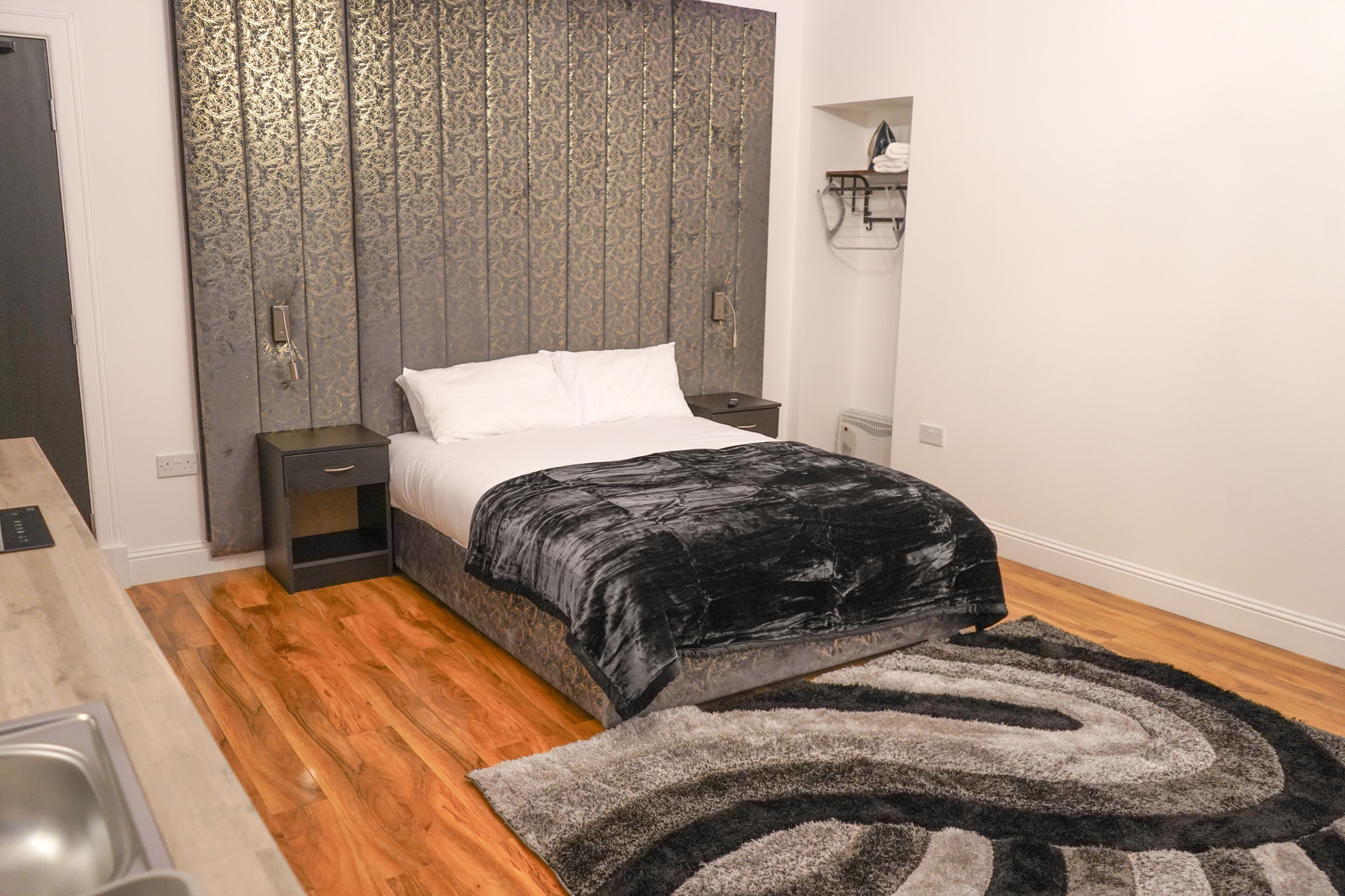 A modern bedroom with a large bed, a nightstand, a dresser, and a wooden floor.
