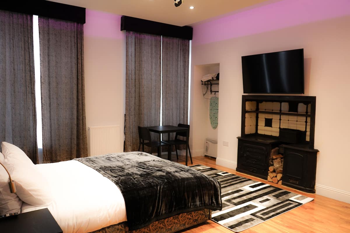 Un dormitorio con cama, escritorio, televisor y chimenea.